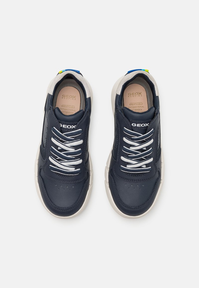 Zapatillas de piel azul marino con cordones blancos, suelas color crema y un acento azul en el talón. Incluyen perforaciones para transpirabilidad.