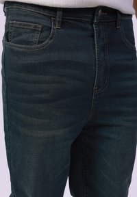 Jeans de mezclilla azul oscuro con una textura suave, diseño de cinco bolsillos y costuras en contraste a lo largo de las costuras y bolsillos.