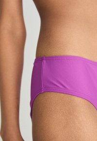 Parte de baixo de biquíni roxa feita de tecido suave, apresentando um design de cintura baixa e detalhes de costura mínimos nas laterais.