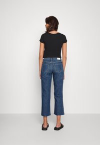 Top preto de mangas curtas e jeans de ganga azul de cintura alta com bainha desfiada e cinco bolsos, usados com sapatos pretos de escorregar.