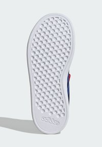 Witte Adidas schoenzool met hexagonaal loopvlakpatroon en het Adidas-logo nabij de hak, die een schaduw werpt op een lichte achtergrond.