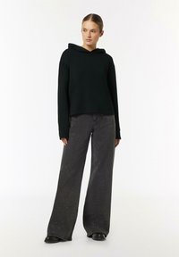 Czarna bluza z kapturem o luźnym kroju, zestawiona z szerokimi ciemnymi dżinsami z subtelnym wzorem błyszczącym oraz czarnymi botkami za kostkę.