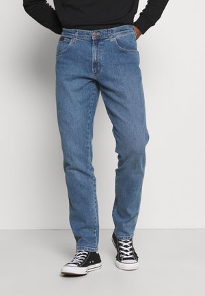 Vaqueros de mezclilla azul claro con corte recto, que cuentan con bolsillos frontales y cierre de botón. Llevados con zapatillas altas negras.
