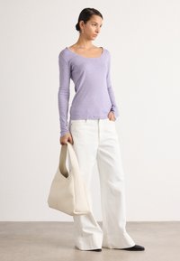Lavendel langermet topp med en rund hals, kombinert med hvite vide bukser og en beige veske. Svarte spisse leiligheter fullfører antrekket.