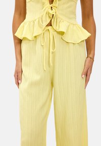 Mono amarillo texturizado con cintura de peplum voladizo y cierre con lazo, que presenta piernas anchas y una tela suave y ligera.