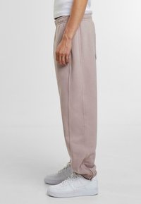 Pantaloni de jogging roz deschis cu talie elastică, buzunare laterale și un croi lejer, asortați cu adidași albi. Textură netedă.