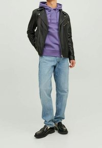 Svart läderbikerjacka över en lila huvtröja, ljusblå jeans och svarta skor med texturerad yta och kraftiga sulor.