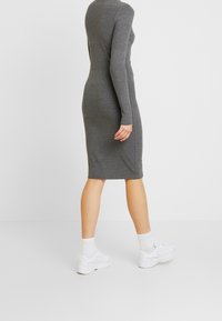 Vestito a maglia grigio con coste, caratterizzato da una silhouette aderente e maniche lunghe, che arriva a metà polpaccio, abbinato a sneaker bianche e calze.