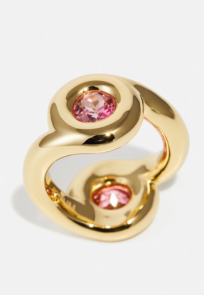 Anello in metallo color oro con un design curvo e liscio, caratterizzato da due gemme rosa sfaccettate incastonate in accenti circolari rialzati.