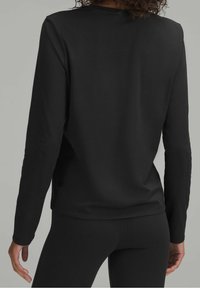 Czarna bluzka z długim rękawem o gładkiej fakturze, z okrągłym dekoltem i dopasowanym krojem, w zestawieniu z czarnymi legginsami.