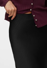 Zwarte rok met een zachte, gestructureerde afwerking, gecombineerd met een bordeauxrode ribgebreide top met zilveren knopen aan de zijkant.