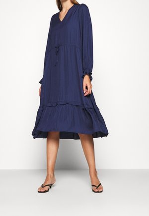 Robe bleu marine, longueur genou, avec des plis verticaux, col en V, manches longues, taille à cordon et détail de volant à l'ourlet.