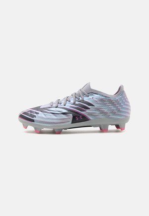 Lichtgrijze voetbalschoen met roze accenten, gestructureerd patroon, veters en gevormde noppen op de zool tegen een witte achtergrond.