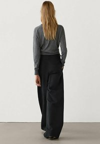 Grijze langmouwen top en losse zwarte broek. Zacht stof, relaxte pasvorm en eenvoudig ontwerp. Broek heeft zijzakken en knopen.