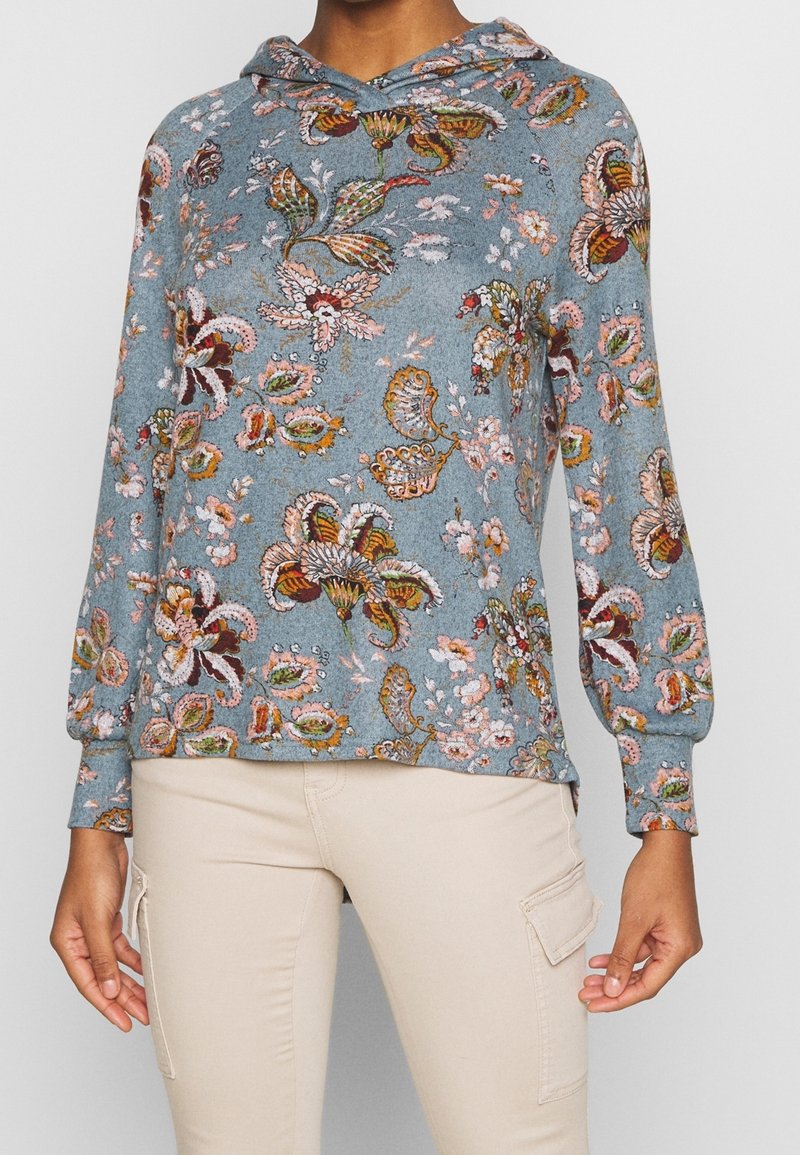 Mikina s kapucí z světle modré látky s květinovým vzorem v oranžové, růžové a zelené barvě. Dlouhé rukávy se staženými manžetami. Pohodlný střih.