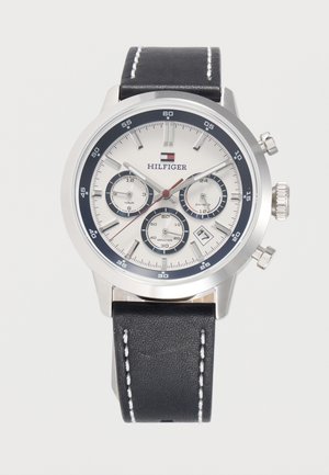 Srebrny zegarek chronograf Tommy Hilfiger z białą tarczą, trzema subtarczami, okienkiem daty, czarnym paskiem skórzanym i białym przeszyciem.