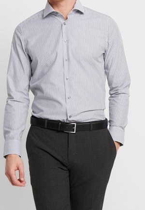 Camicia a maniche lunghe con bottoni a strisce sottili blu e bianche, in tessuto di cotone, colletto classico, abbinata a pantaloni grigi e una cintura nera.