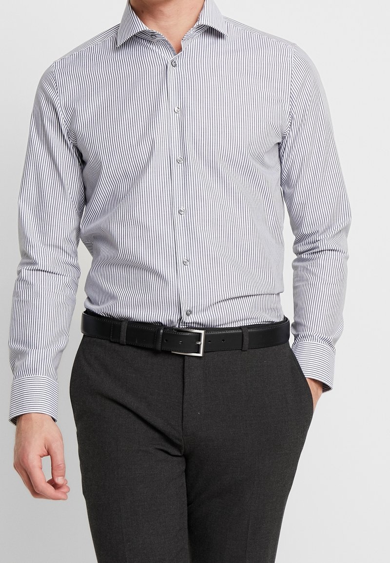 Långärmad skjorta med knappar i tunna blå och vita ränder, i bomull, klassisk krage, i kombination med grå byxor och ett svart bälte.