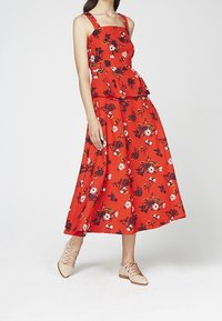 Czerwona sukienka w kwiaty z dopasowanym górnym partem, detalem peplum oraz szeroką spódnicą. Posiada ramiączka i różnorodne kolorowe wzory kwiatowe.