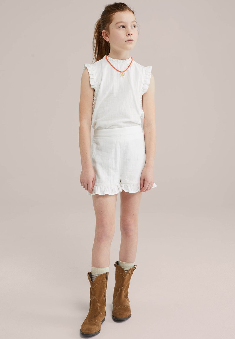 White linen top with ruffled sleeves, paired with white linen shorts featuring a frilled hem. Brown suede cowboy boots with sock accents.