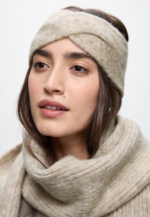 Beige uldehælde med et snoet design, der har en blød tekstur. Blev parret med et matchende chunky tørklæde, også i beige.