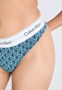 Calvin Klein bikini i blått med geometriskt mönster, vit logoband. Materialet verkar slätt och elastiskt med en figurnära design.