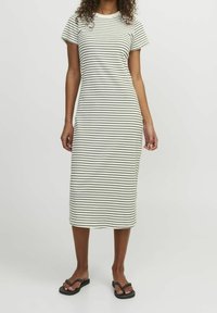 Robe midi rayée en crème et noir, en tissu côtelé. Caractéristiques : manches courtes et décolleté rond. Portée avec des tongs noires.