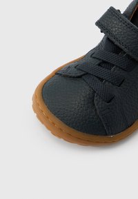 Παπούτσι από δέρμα σε ναυτικό μπλε με υφή, στρογγυλή μύτη και καφέ σόλα από καουτσούκ. Διαθέτει λουράκι με βέλκρο και σχέδιο με κορδόνια για ασφαλή εφαρμογή.