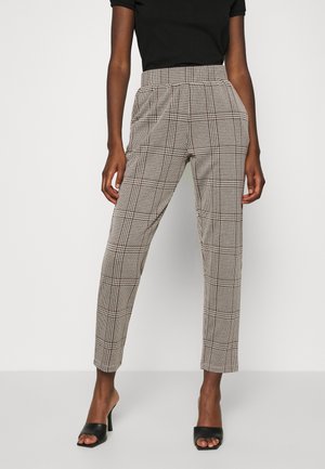 Mujer con pantalones de cintura alta beige y negro a cuadros, combinados con una camiseta negra de manga corta y sandalias negras de tacón abiertas.