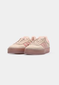 Helle rosa Wildleder-Sneaker mit drei dunkleren rosa Streifen, runder Zehenpartie und transparentem rosa Gummisohle. Glatte Textur überall.