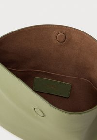 Zaļa ādas soma ar gludu faktūru, ar brūnu zamša oderi un logotipa etiķeti. Satur apaļu aizdares elementu ar spiedpogu.