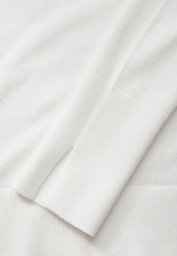 Weißer Strickstoff mit glatter Textur. Das Design umfasst einen gerippten Saum und Bündchen mit dezenten Nahtdetails und seitlichem Schlitz.