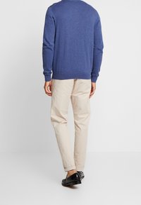 Niebieski dziany sweter z okrągłym dekoltem, zestawiony z beżowymi chinosami i czarnymi eleganckimi butami, widziany od tyłu. Gładka faktura, luźny krój.