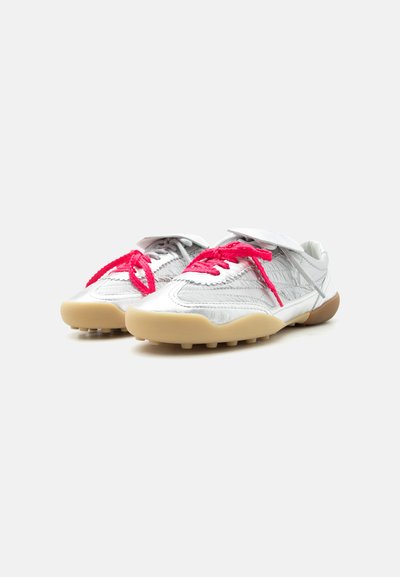 Paire de chaussures de sport blanches avec semelles texturées et lacets rouges vifs sur fond blanc.