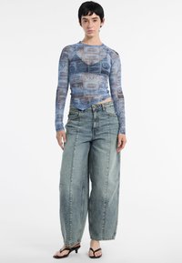 Langermige, doorzichtige, blauwe top met gedrukte grafische details, gecombineerd met losse lichtdenim jeans, met een hoge taille en wijde pijpen.