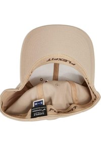 Beige pet met een gebogen sportvizier, gemaakt van zachte stof. Binnenin bevat het een zachte voering en maatlabel. Inclusief stiksels en ventilatiegaten.