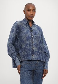 Denim shirt in dark blue with floral print, featuring a button-up design, pointed collar, and long, loose sleeves. Textured fabric.