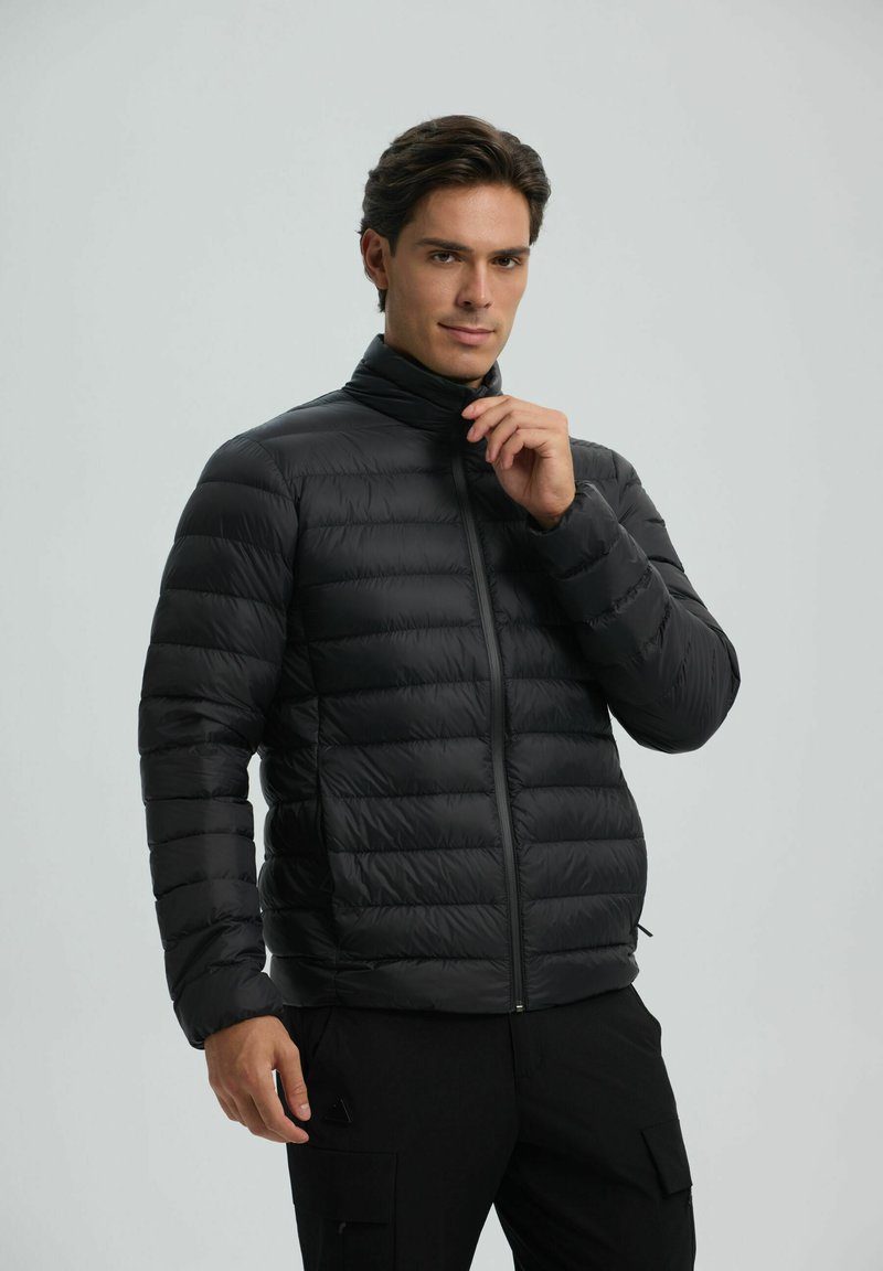 Black puffer jacket with a high collar, quilted design, and zipper closure. The fabric appears glossy and lightweight.