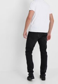 Svarta, figurnära jeans med midja i normalhöjd, fem fickor och en ren design. Bärs med en enkel vit t-shirt och svarta skor.