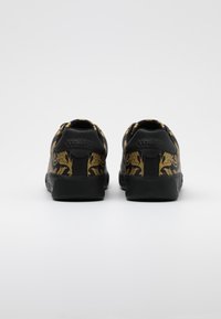 Black sneakers with a gold floral pattern, featuring a smooth texture, rounded shape, and logo detailing on the heel.