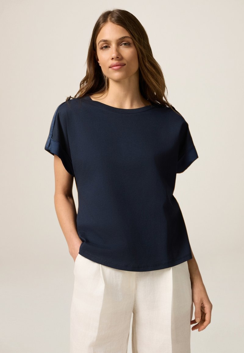 Top de manga corta azul marino con escote redondo, que presenta un corte relajado y material de algodón suave. Combinado con pantalones de lino de color claro.