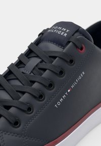 Zapatillas sintéticas navy con suela blanca, presentan un cierre de cordones oscuro en la parte delantera, logo en el lateral y detalles rojos cerca de los ojales y la suela.
