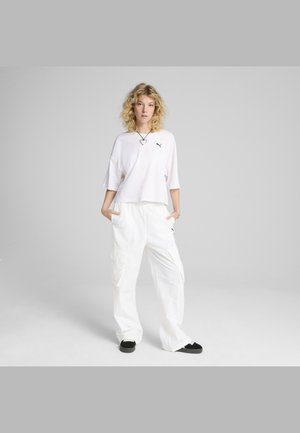 Witte, cropped t-shirt met zwart logo, gecombineerd met losse witte cargobroek met zijzakken, en zwarte instap schoenen.