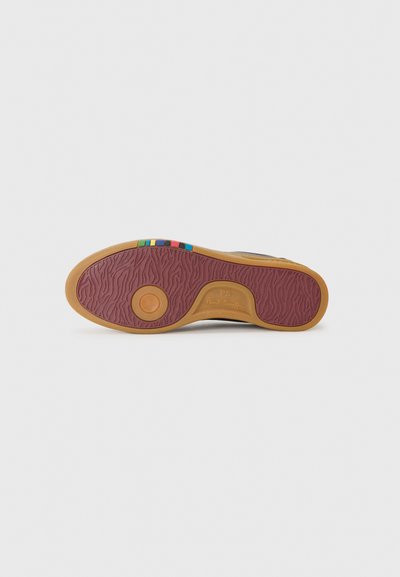 Semelle de chaussure en caoutchouc brun texturé, dotée d'un détail circulaire et de rayures colorées en bleu, jaune, vert et rose.