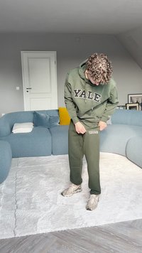 Zelená mikina s kapucňou a tepláky s výrazným nápisom "Yale" v bielych písmenách. Tkanina vyzerá jemne; zostava má uvoľnený strih. Neutrálny pozadie.