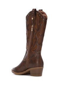 Botas de vaquero de piel marrón con costuras decorativas, cremallera lateral y acentos de tachuelas; cuenta con un tacón apilado y punta redondeada.