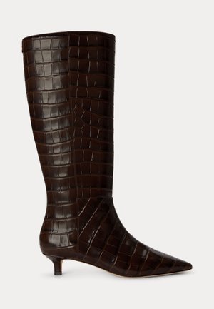 Botte en cuir brun foncé montant jusqu'au genou avec motif crocodile, bout pointu et petit talon kitten, vue de côté sur fond uni.