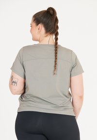 Grå kortärmad skjorta med avslappnad passform, som har en slät yta och horisontella sömsdetaljer, kombinerad med svarta leggings.