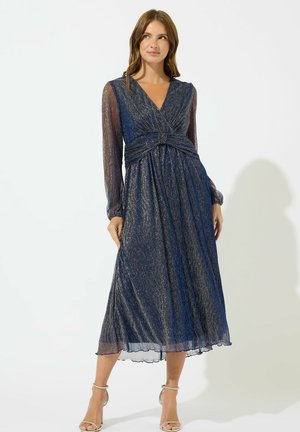 Vestido azul marino de largo completo con mangas largas de tela transparente, un cuerpo retorcido y acentos de hilo metálico. Textura de tela suave y fluida.