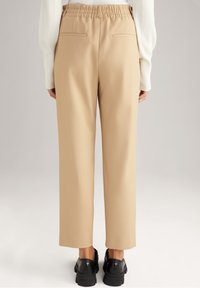 Beżowe spodnie o szerokich nogawkach z wygodnym elastycznym pasem i dwiema kieszeniami z tyłu, zestawione z czarnymi butami. Gładka tekstura materiału.
